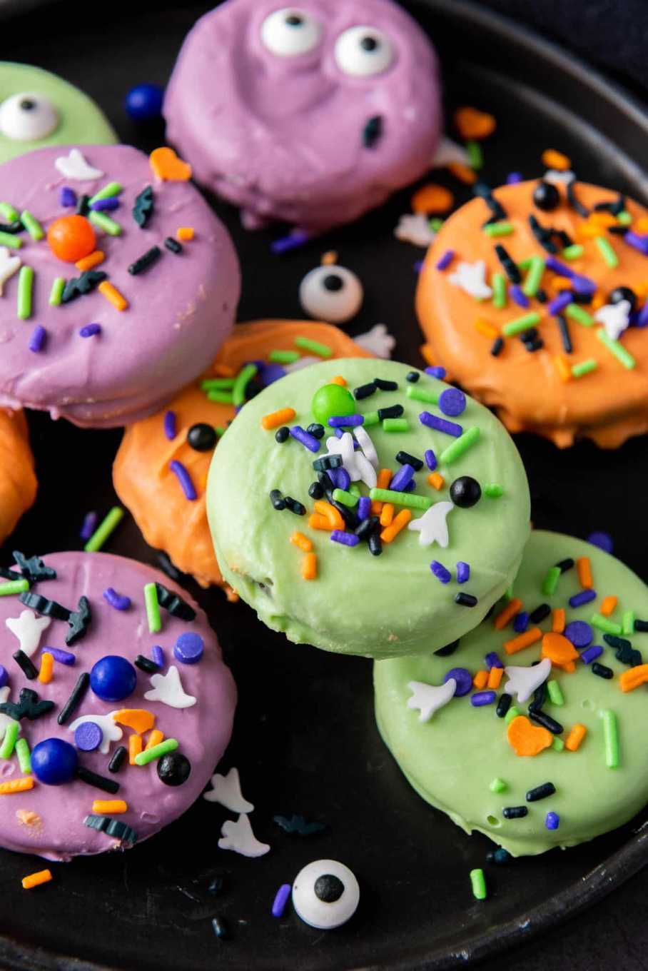 Oreo cookies filled with orange cream, dipped in chocolate, and decorated with black sprinkles on a dark platter